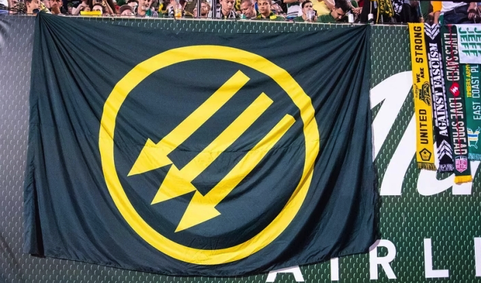 Photo of a large three arrows flag in Portland Timbers colors unfurled at a Timbers game in 2019.